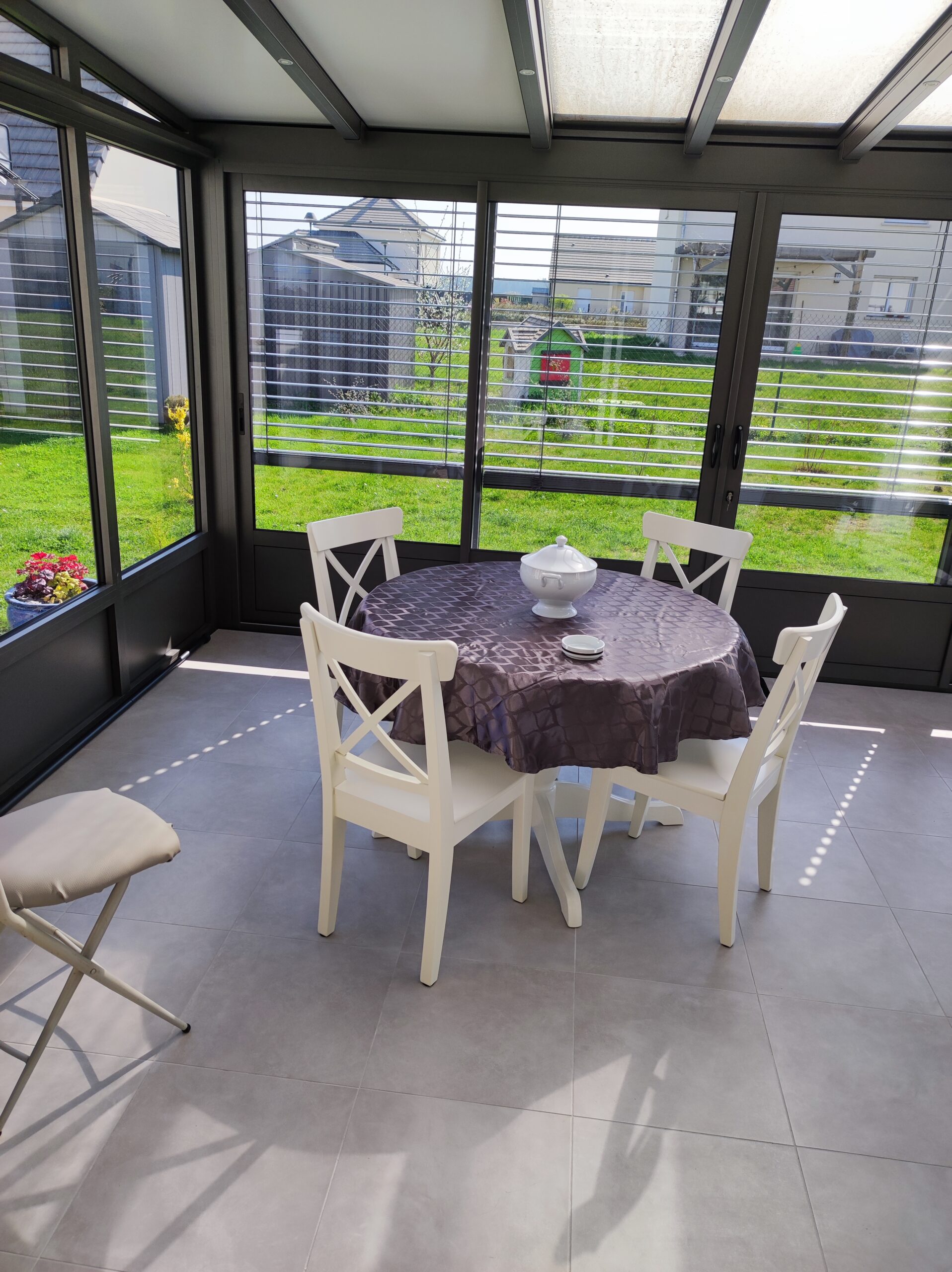 Véranda en aluminium vue de l'intérieur équipé de stores. Sol en carrelage