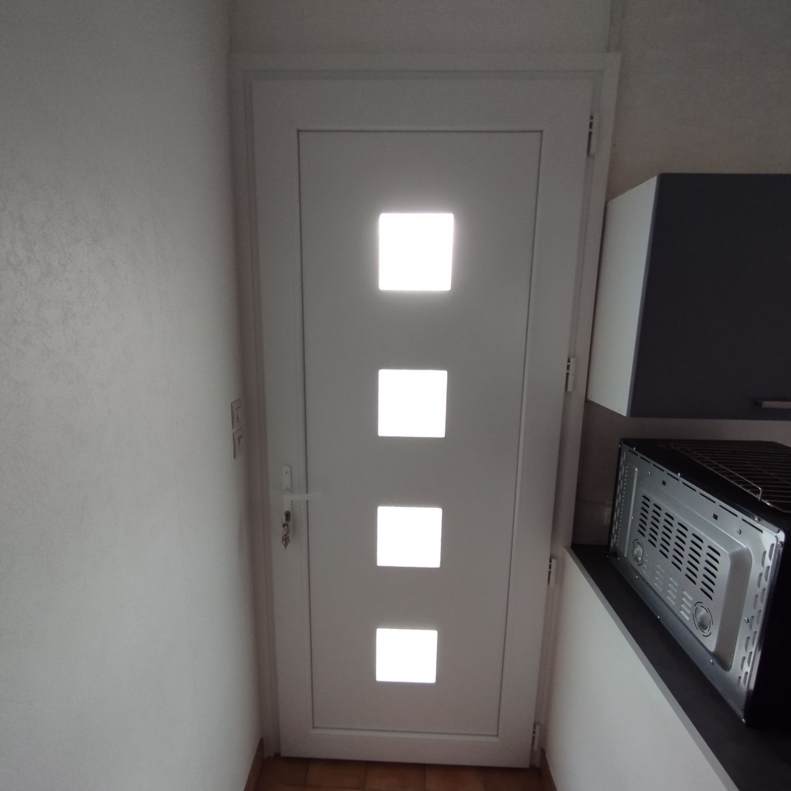 Porte d'entrée avec 4 vitrages carrés pour laisser passer la lumière vue de l'intérieur